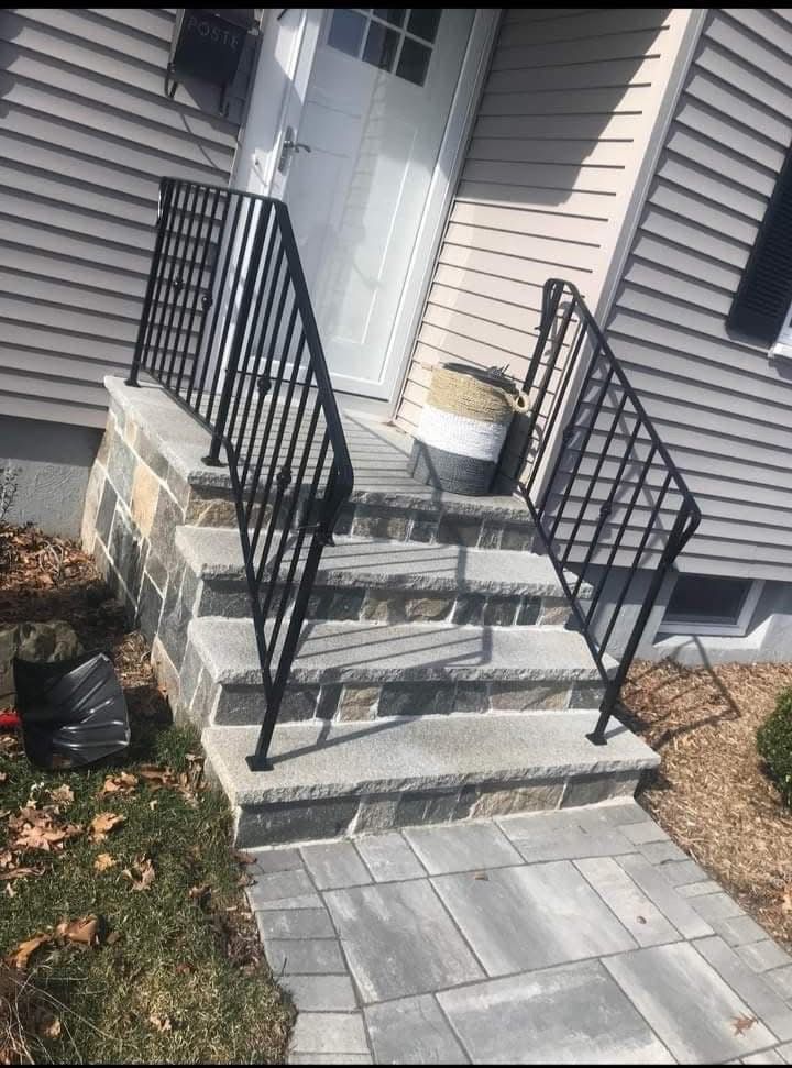 Front steps with black railings leading to a house entrance and gray paver walkway
