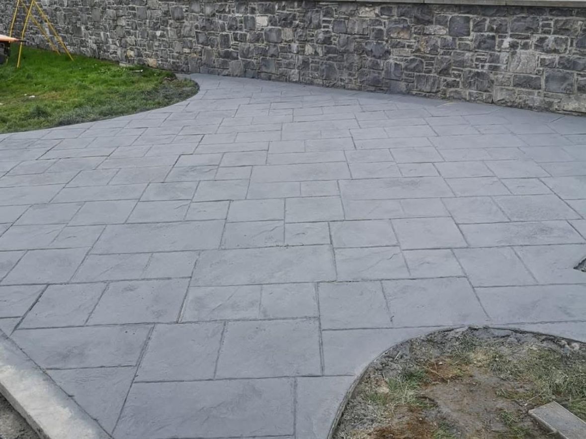 Empty gray stone-paved courtyard beside a stone retaining wall and grass edges