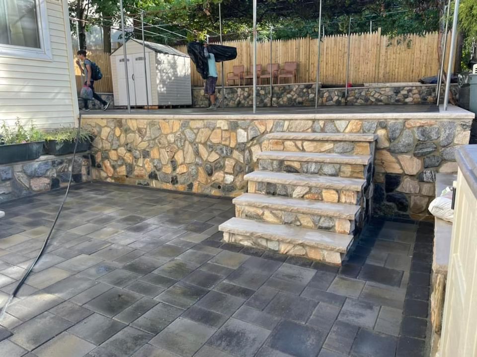 Stone patio with steps leading to a raised deck and fenced backyard seating area