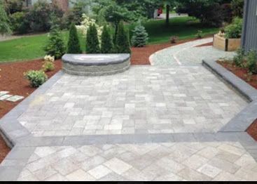 Paved stone patio and walkway in a landscaped garden with shrubs and a circular bench.