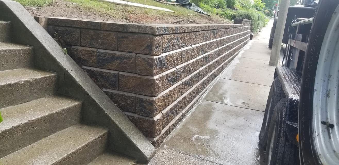 Concrete stairway beside a sloped stone retaining wall and wet sidewalk next to a parked car