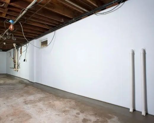 Empty basement with white wall, exposed wooden ceiling beams, and concrete floor