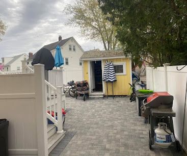 Backyard patio with paver stones, shed, grill, and hanging towels beside a house