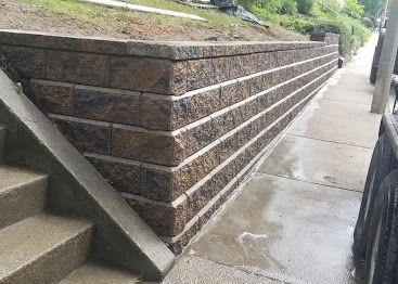 Concrete retaining wall beside a wet sidewalk, with steps at left and a sloped walkway on top