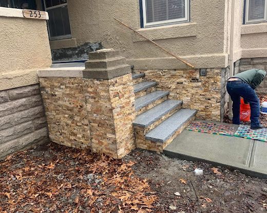 Worker laying pavers beside stone house steps and a concrete walkway