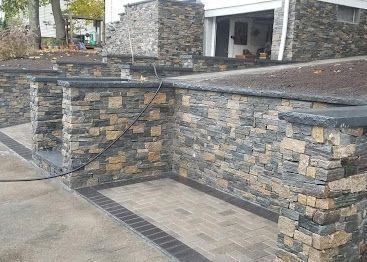 Stone retaining wall and ramp beside a building entrance, with black handrails.