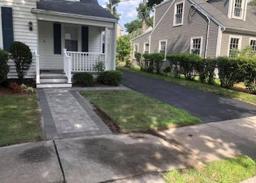 Suburban front yard with a gray walkway, porch, driveway, and two houses on a sunny day