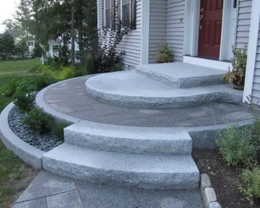 Curved concrete front steps and a raised porch entrance beside a house, with landscaped flower beds.