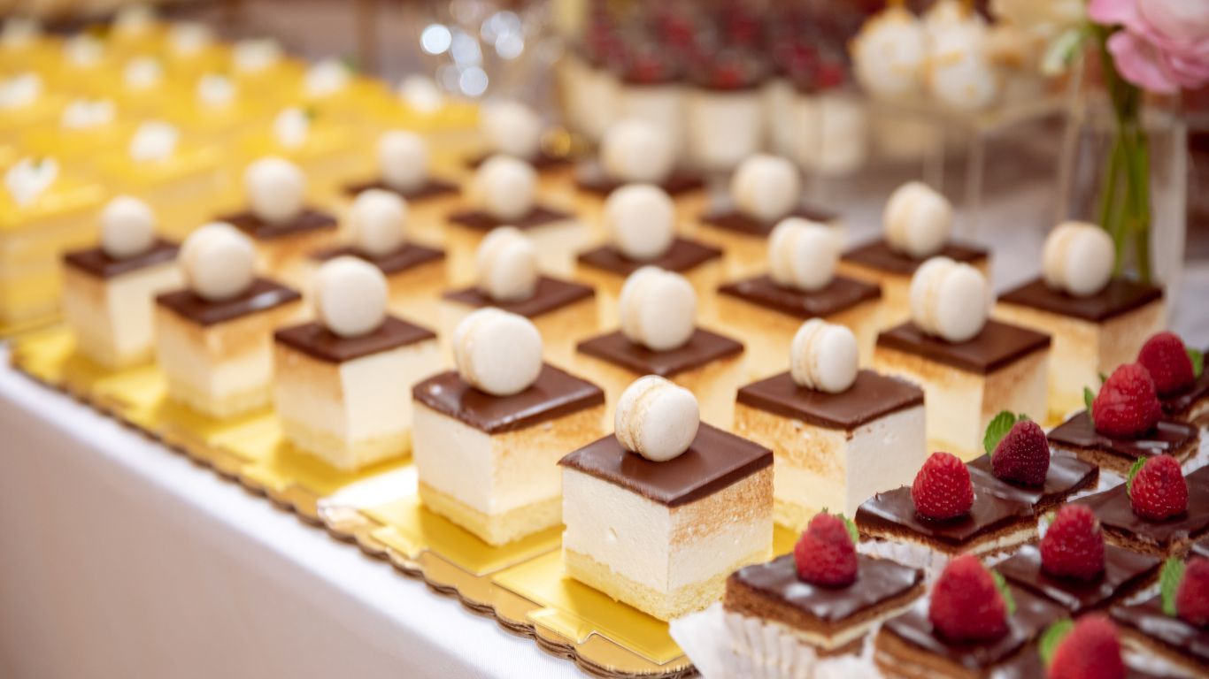 Dessert table with square cakes topped with chocolate, macarons, and raspberries.