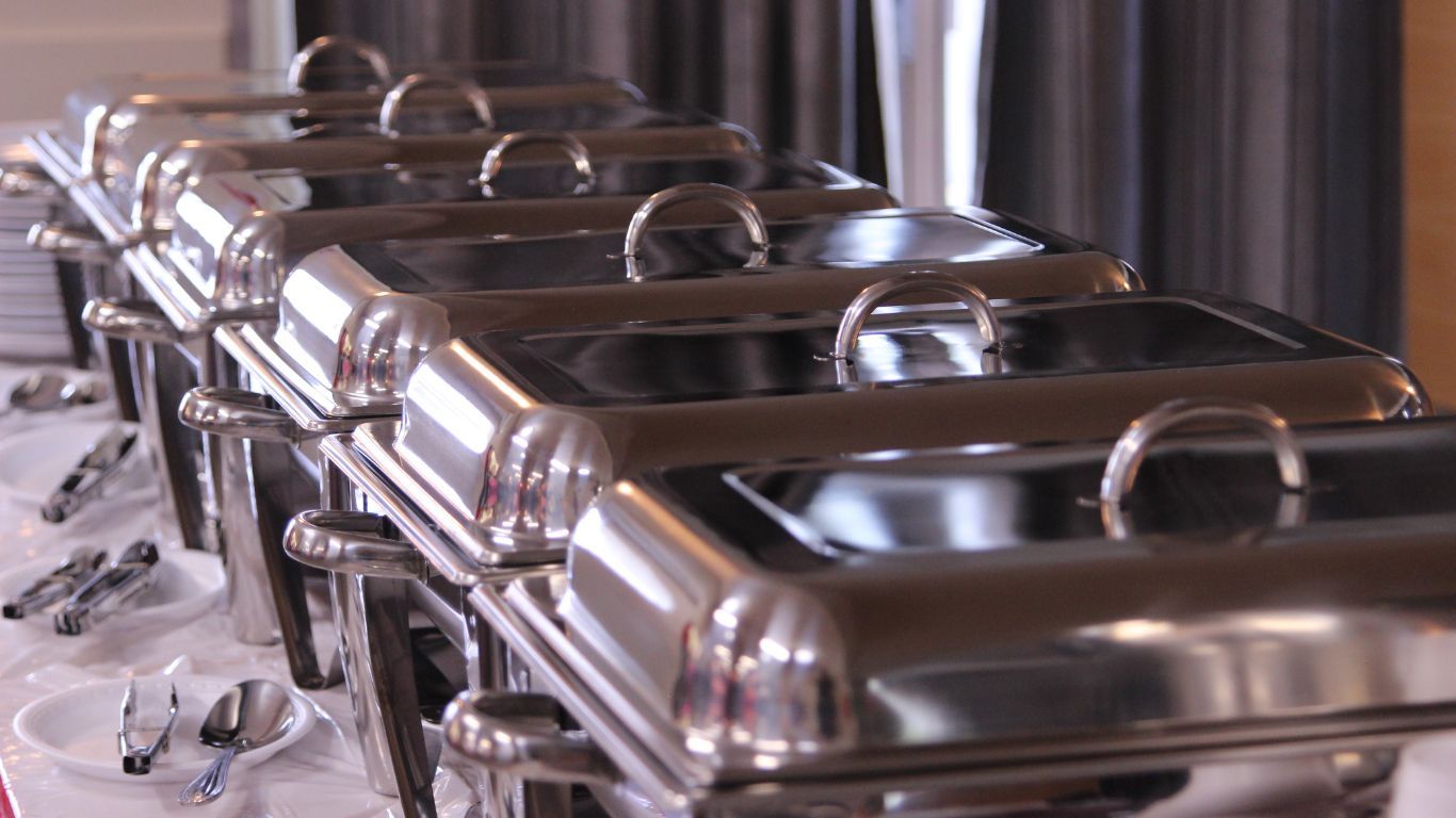 Buffet line with covered stainless steel food warmers on a white tablecloth.