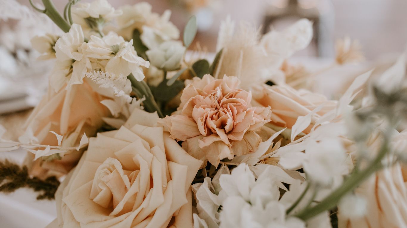 Close-up of a cream and peach floral arrangement with roses and carnations, likely for a wedding.