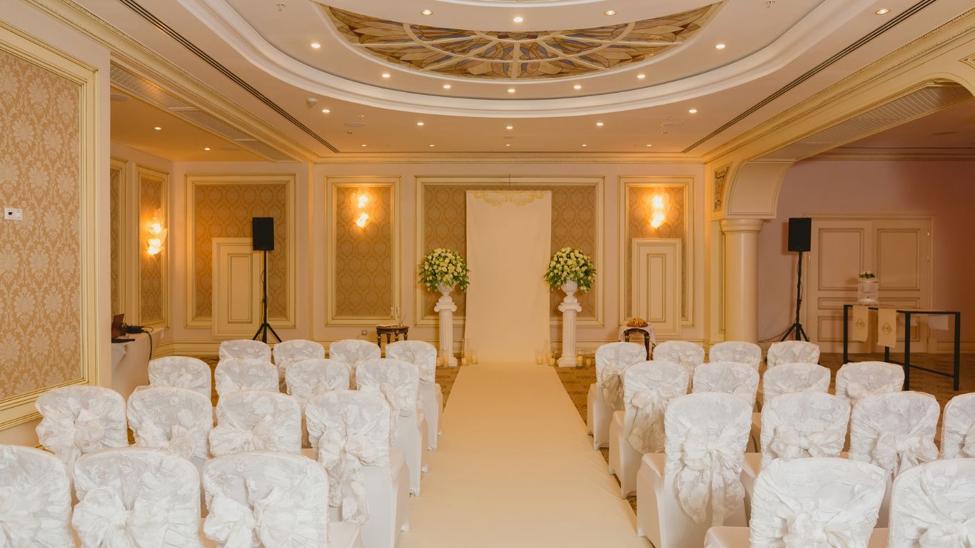 Wedding ceremony setup in a cream-colored ballroom with rows of chairs facing a flower-decorated altar.