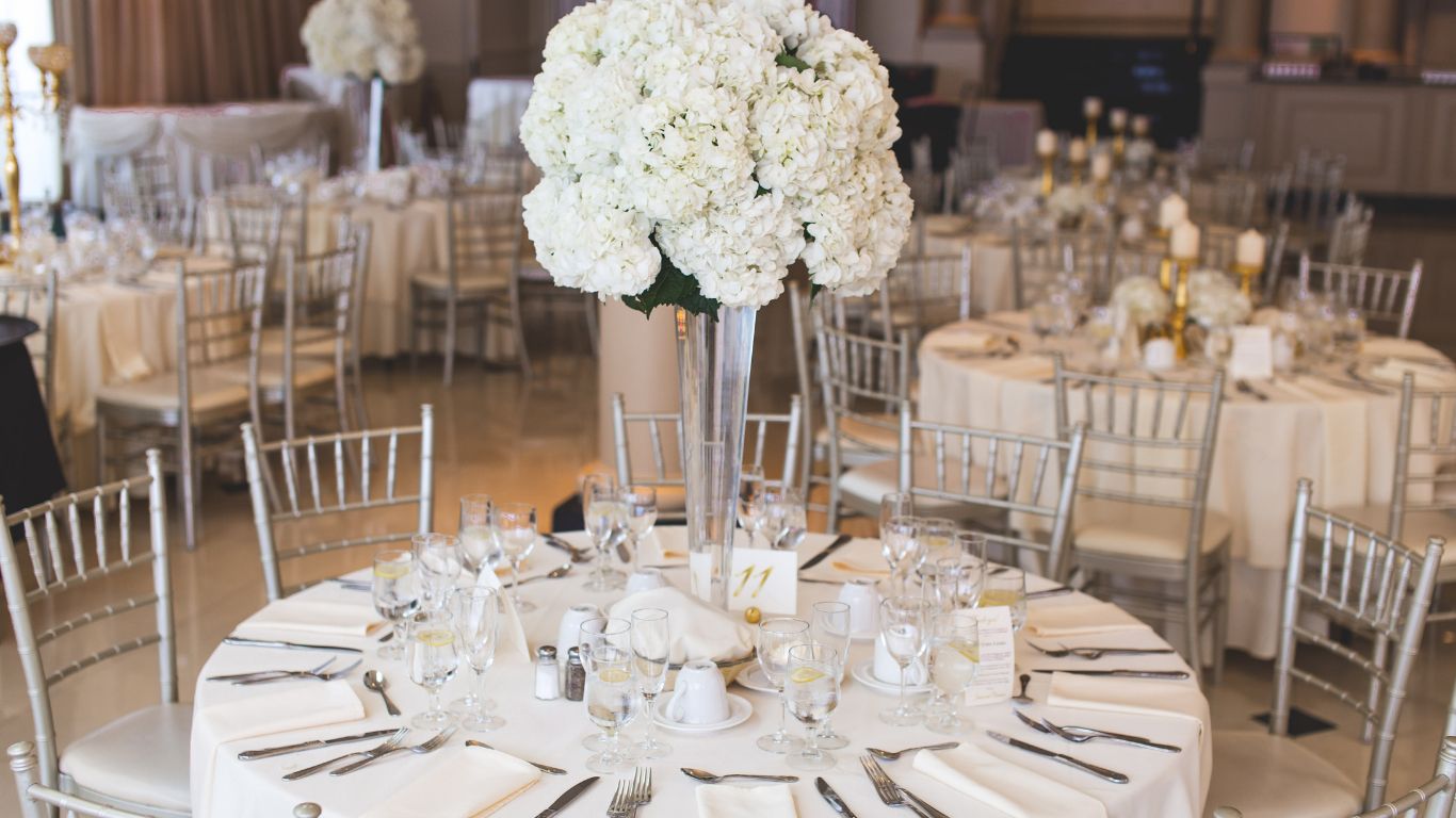 Elegant wedding reception with round tables set for guests, centered around tall floral arrangements.