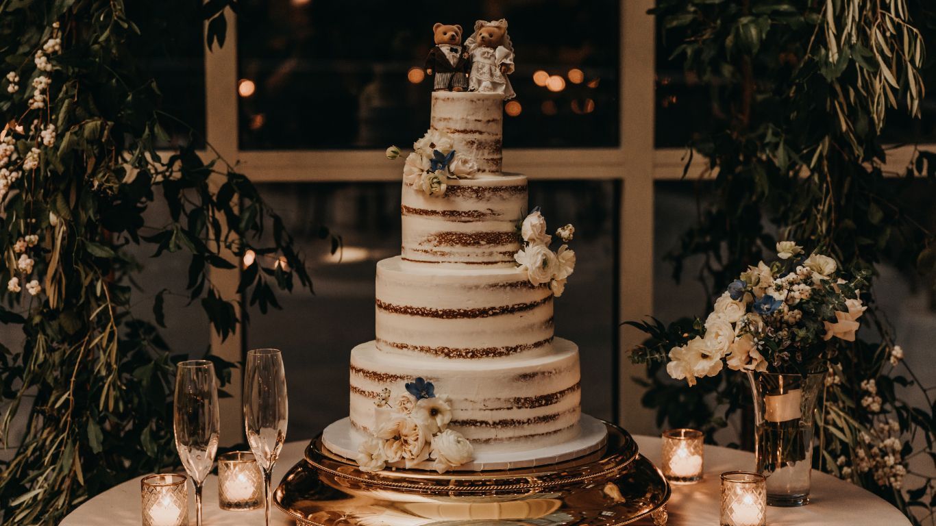 Wedding cake with multiple tiers, flowers, and bear cake toppers at a reception.