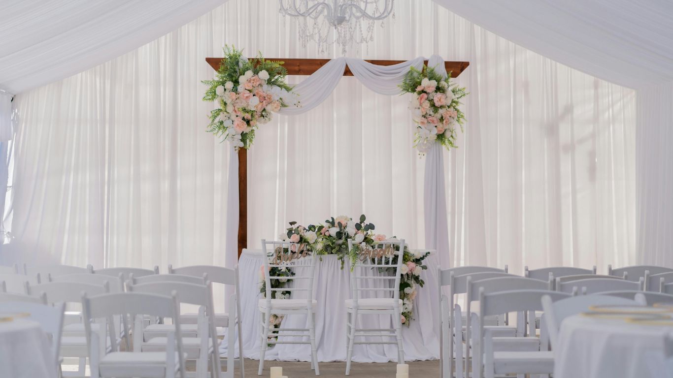White wedding ceremony with floral arch and decorated table.