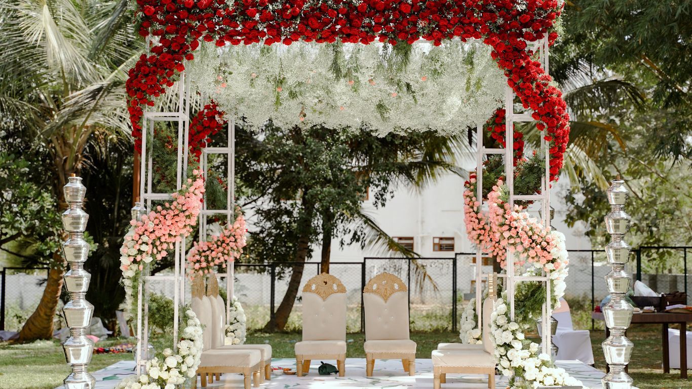 Floral wedding arch with chairs, red and white flowers, outdoor setting.
