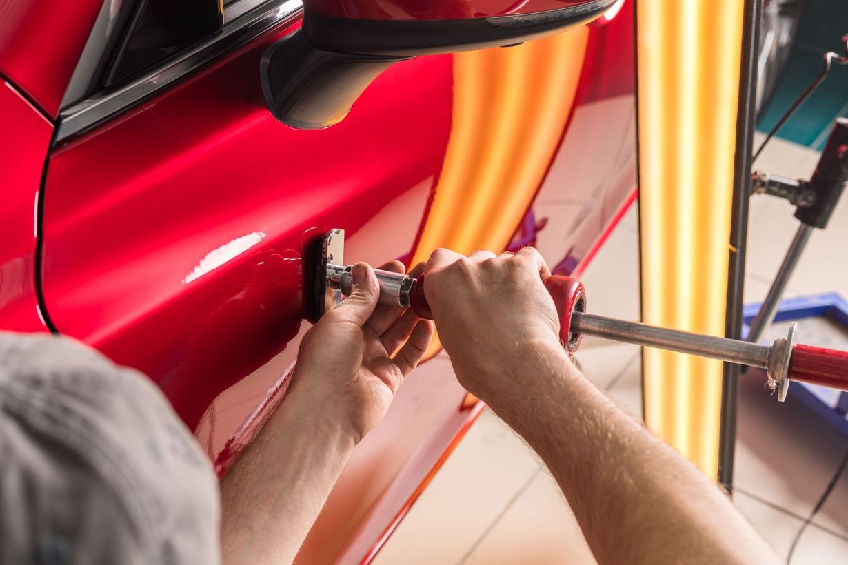 Person using tools to remove a dent from a red car door.