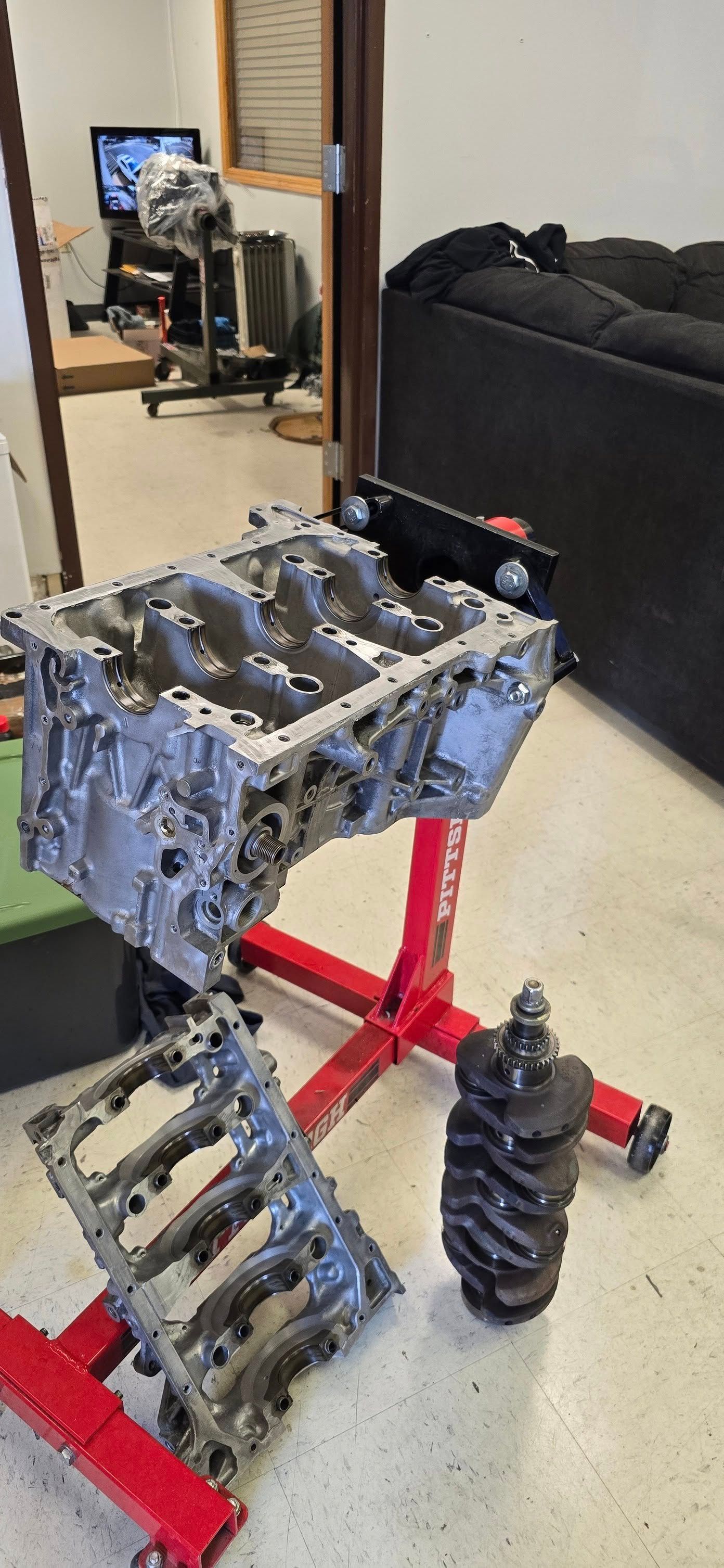 Engine block on a red stand. Crankshaft and bearing caps are next to it.