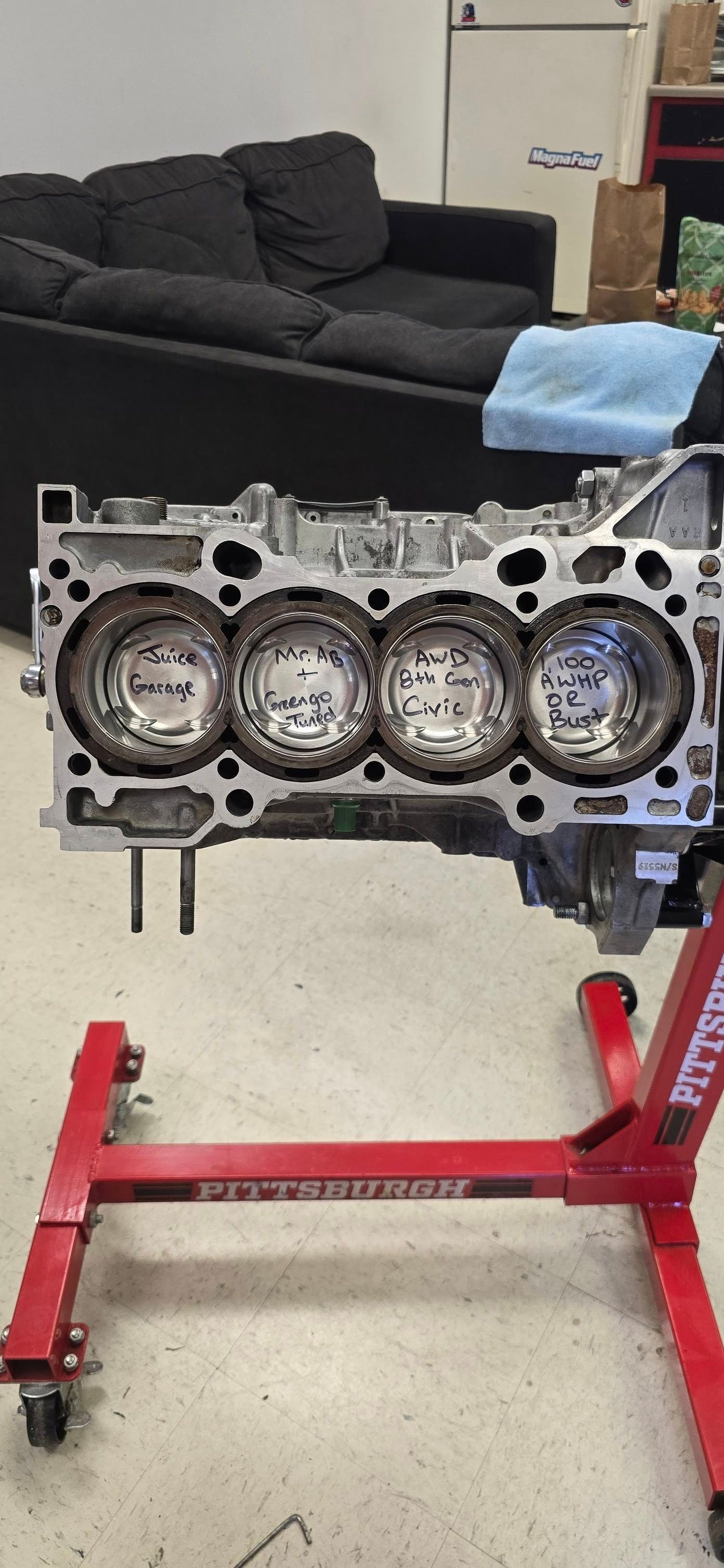 An engine block sitting on a red stand. It has four cylinders, in a workshop setting.