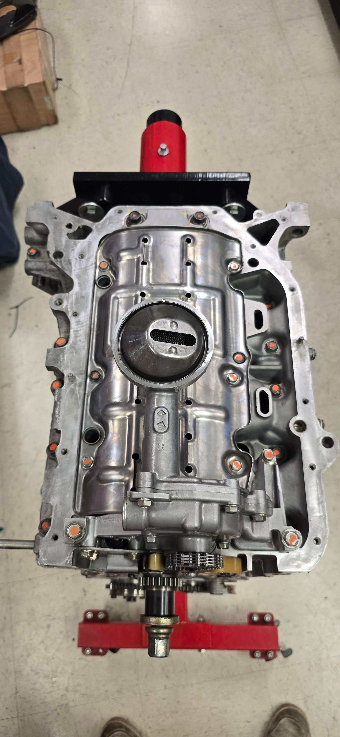 Engine block assembly on a red stand. Silver and gray metal with bolt and gear details. Red support on top.