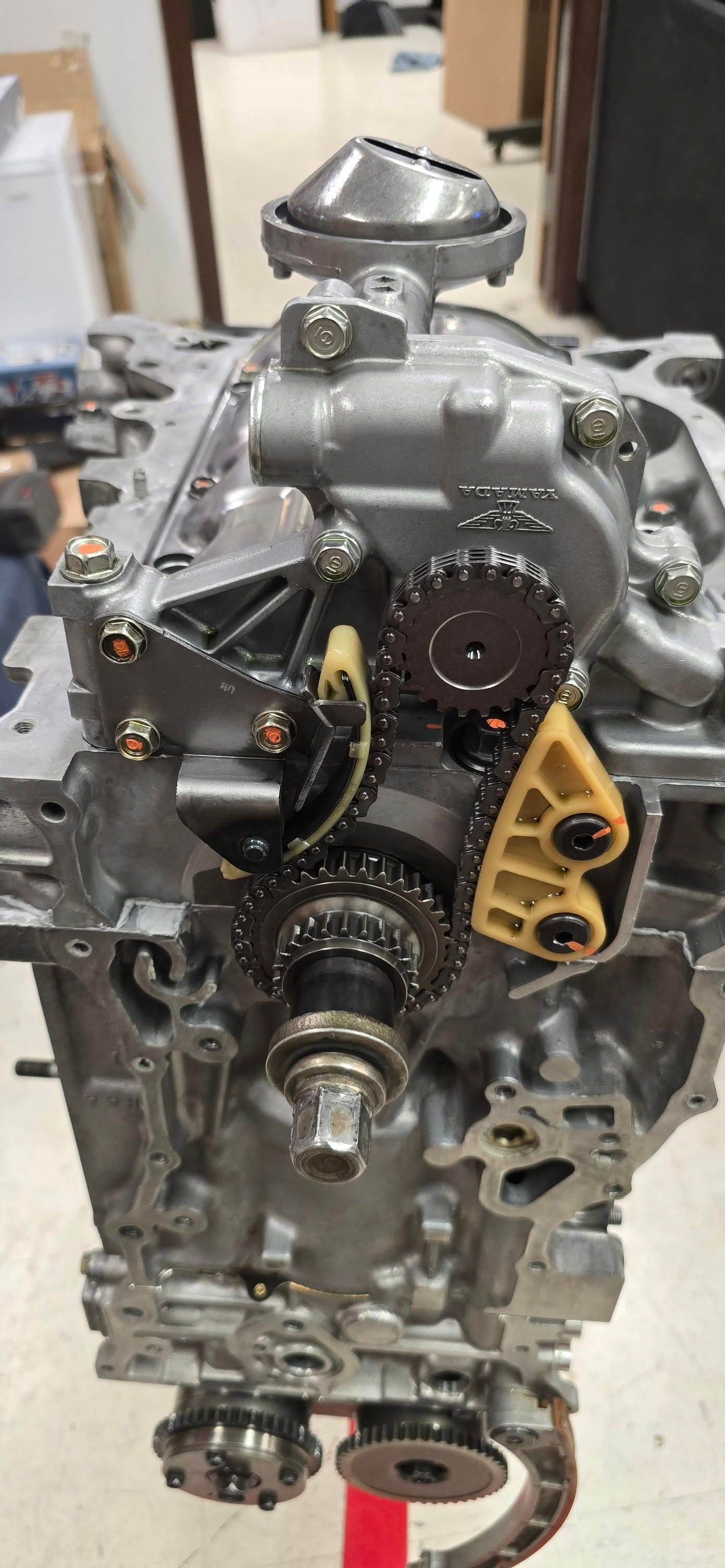 Engine block with gears, chain, and oil pump assembly visible. Silver metal and yellow plastic components.