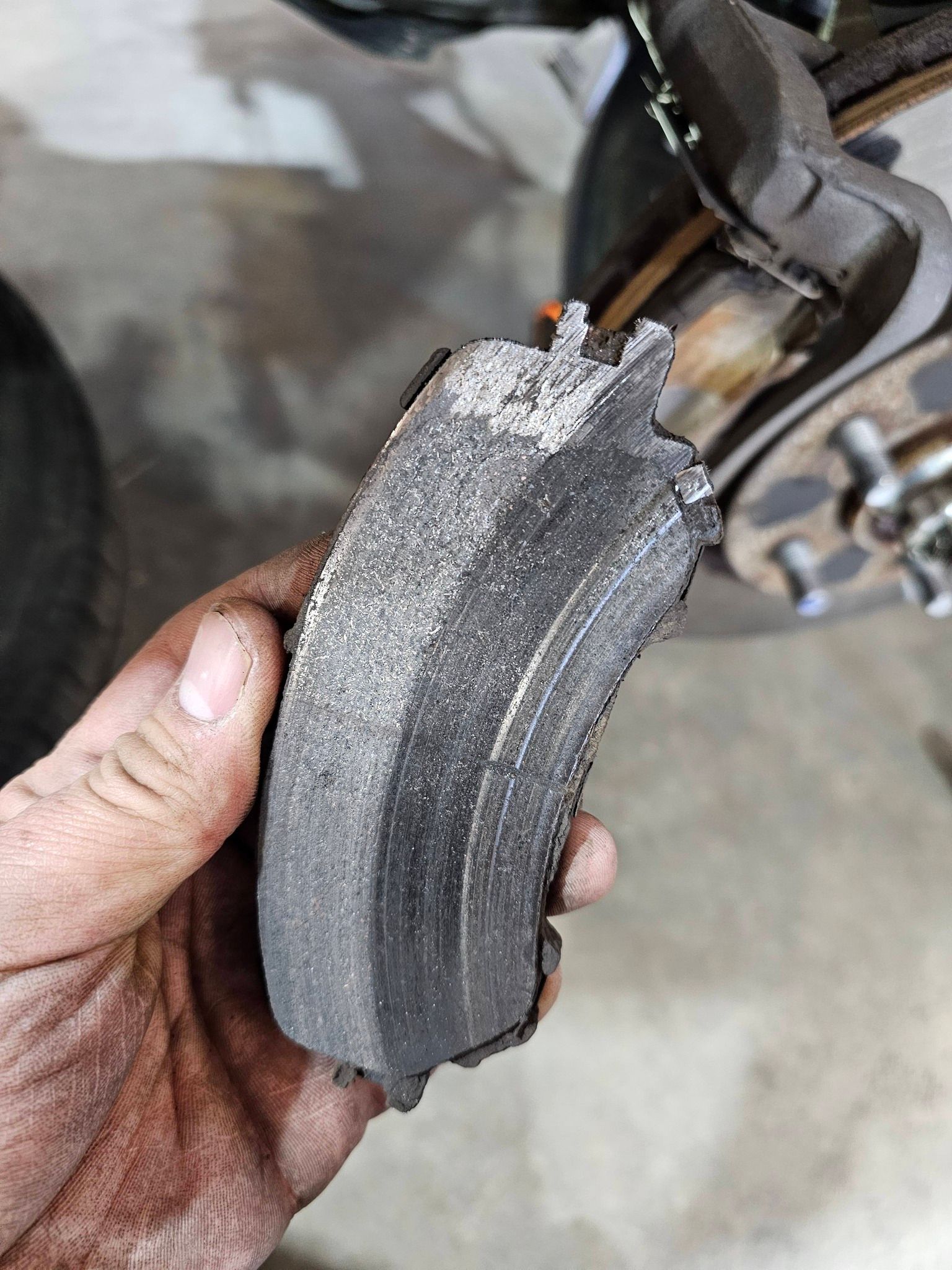Hand holding a severely worn brake pad, near a vehicle's brake system.
