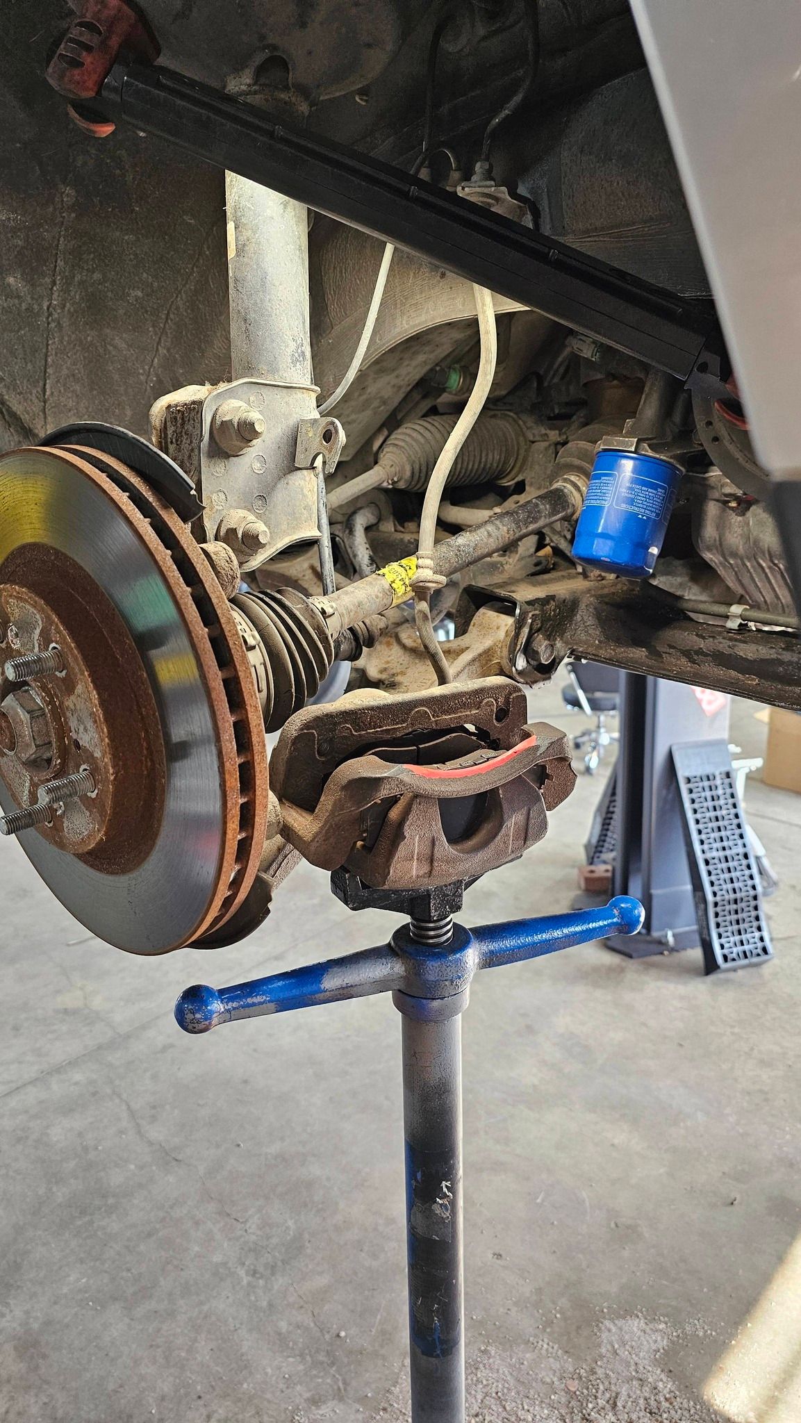 Car's front wheel removed, brake rotor and caliper visible. Vehicle supported by a jack stand.