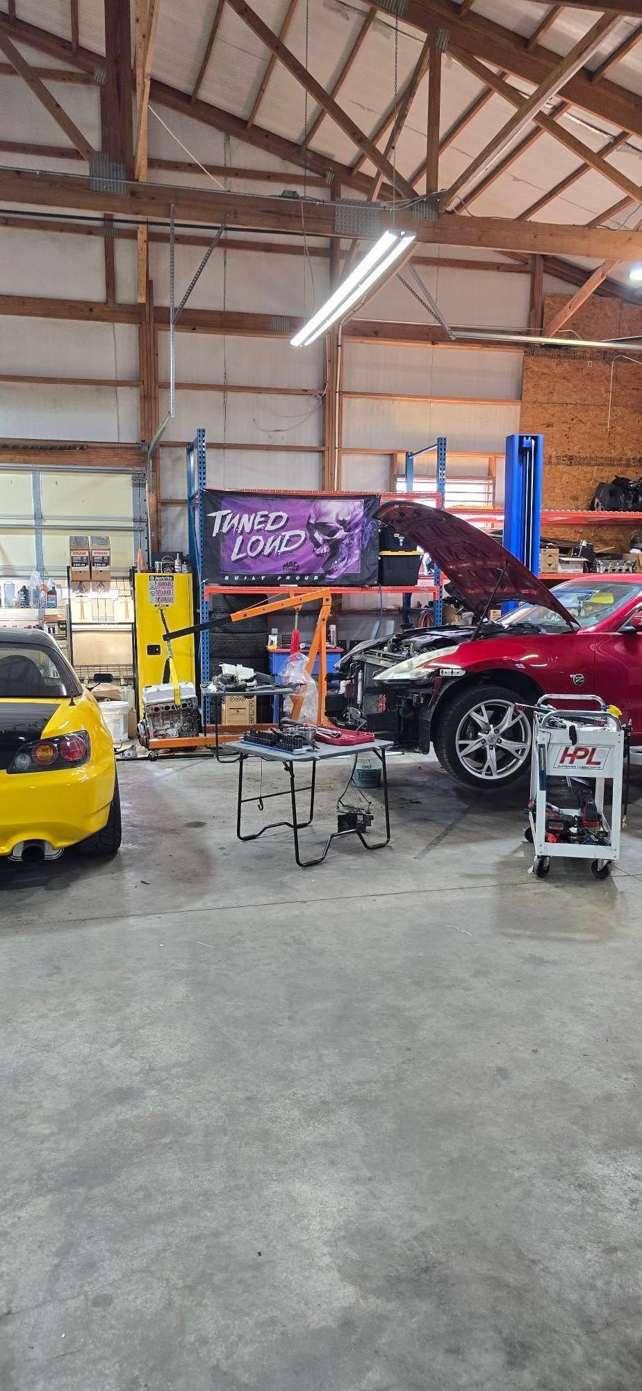 A car repair shop. A yellow sports car and red car are being worked on. Tools and equipment are in the shop.
