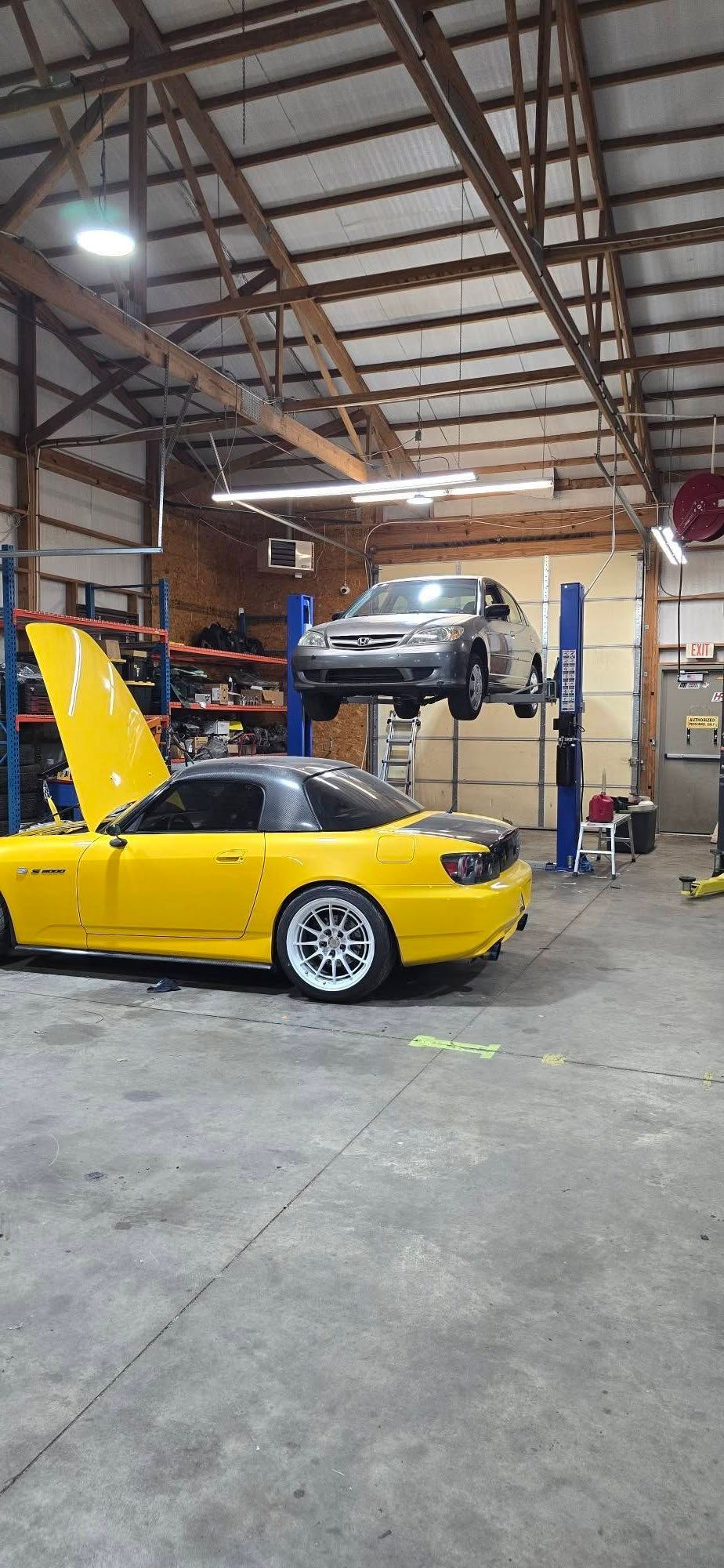 Yellow sports car parked next to a car lifted in an auto repair shop.