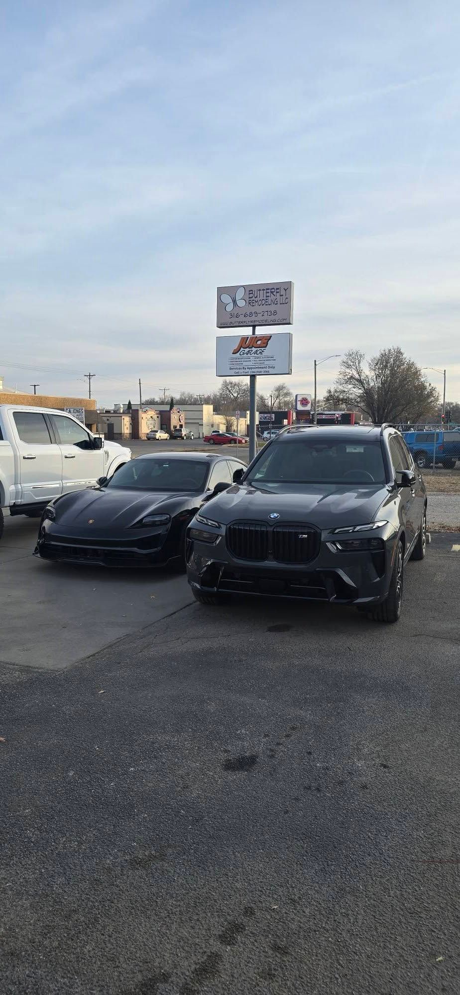 Two black cars parked on gravel in front of a sign; a light sky in the background.