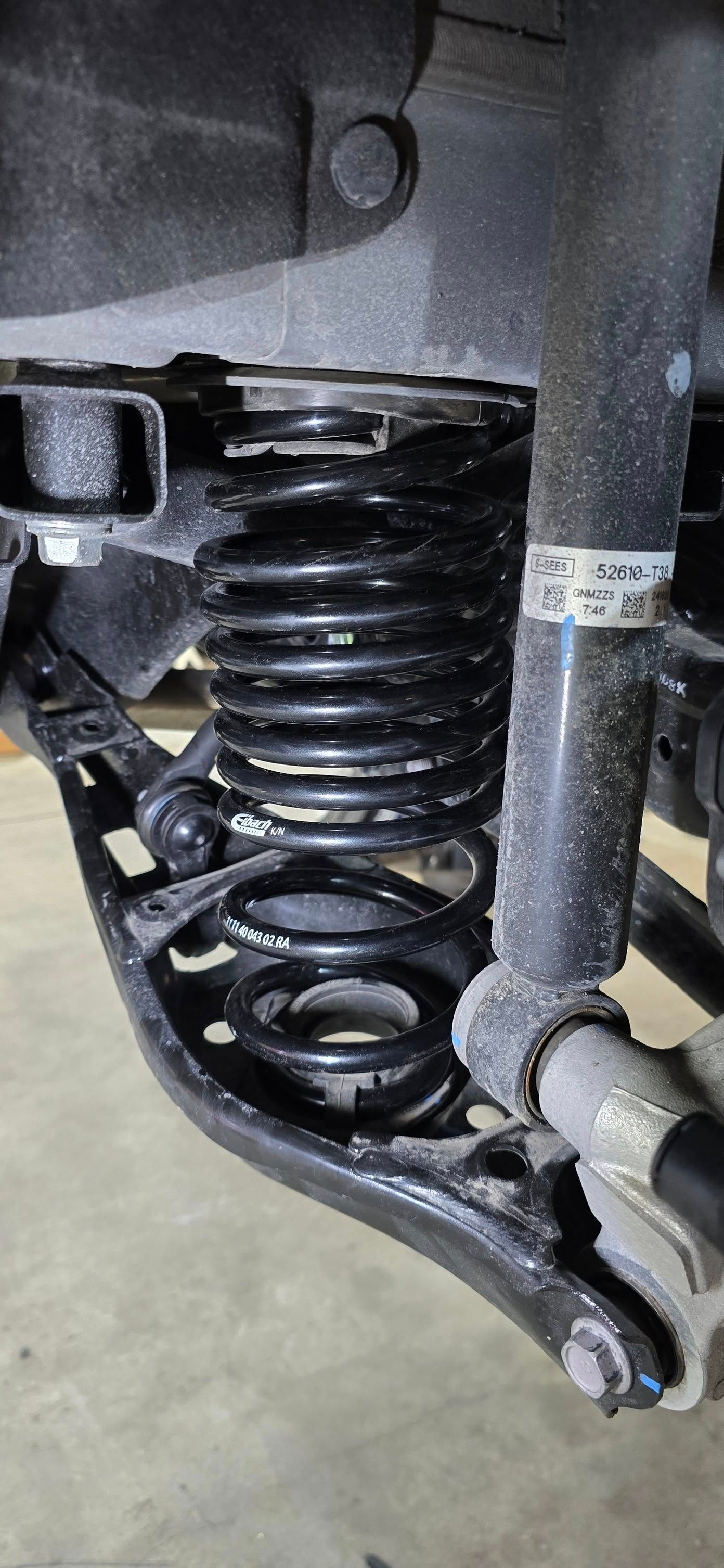 Car suspension system with a black coil spring and shock absorber.