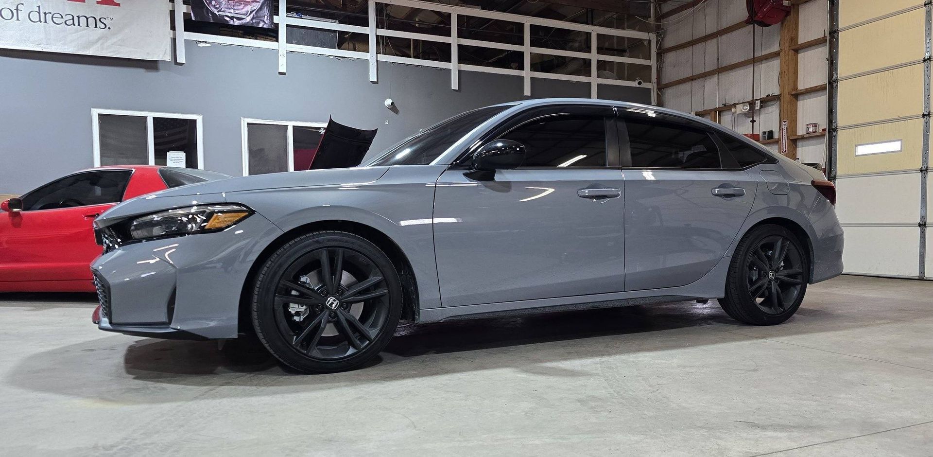 Gray sedan with black rims in a garage next to a red car.