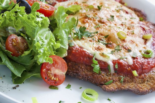 Breaded cutlet with melted cheese, tomato sauce, and a side salad with cherry tomatoes and greens