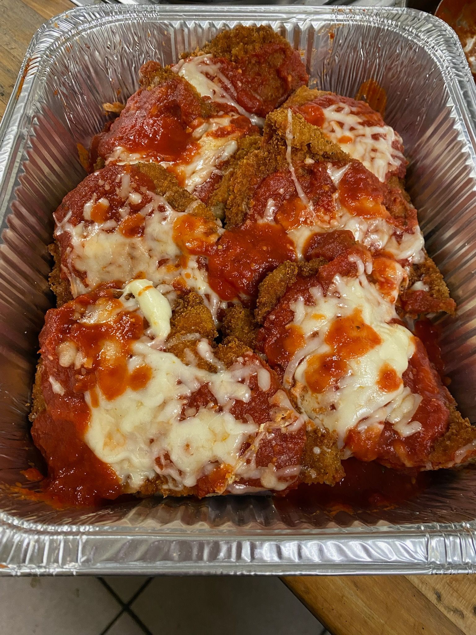 Foil tray of baked pasta with red sauce and melted cheese, topped with sliced pepperoni