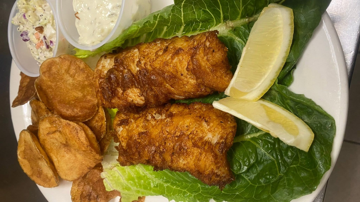 Plate of fried fish with lemon wedges, roasted potatoes, and creamy dipping sauce on lettuce garnish