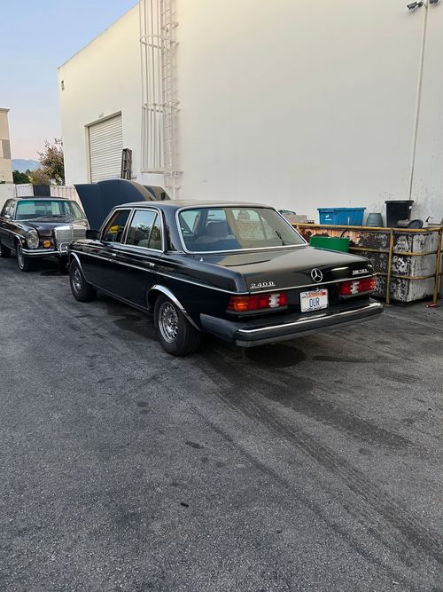 Classic black convertible parked in an alley beside a white building, with another car behind it.