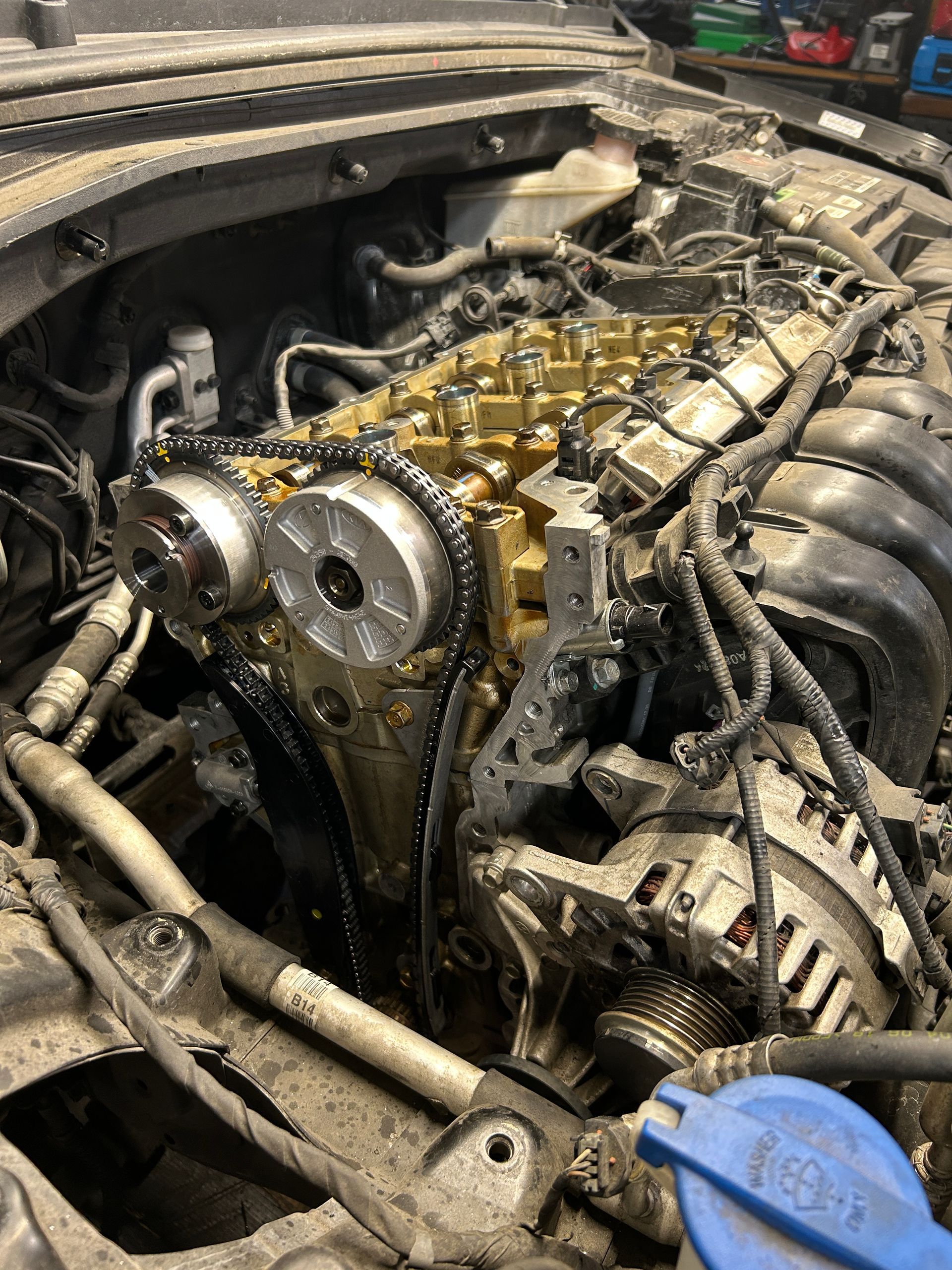 Open car engine with exposed timing components, hoses, and a blue cap in a dusty repair bay