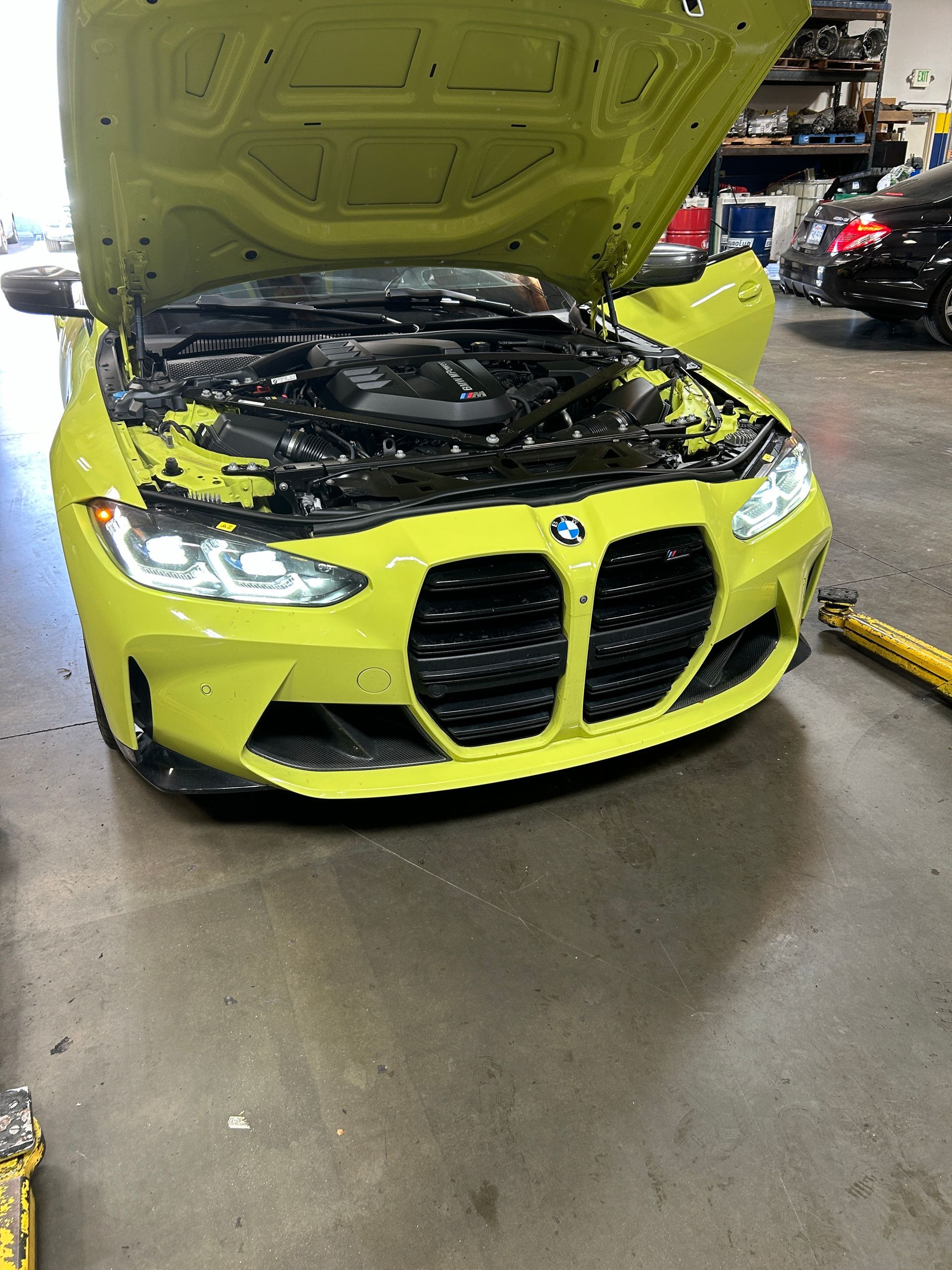 Bright yellow BMW with hood open in an auto repair shop, front damage visible