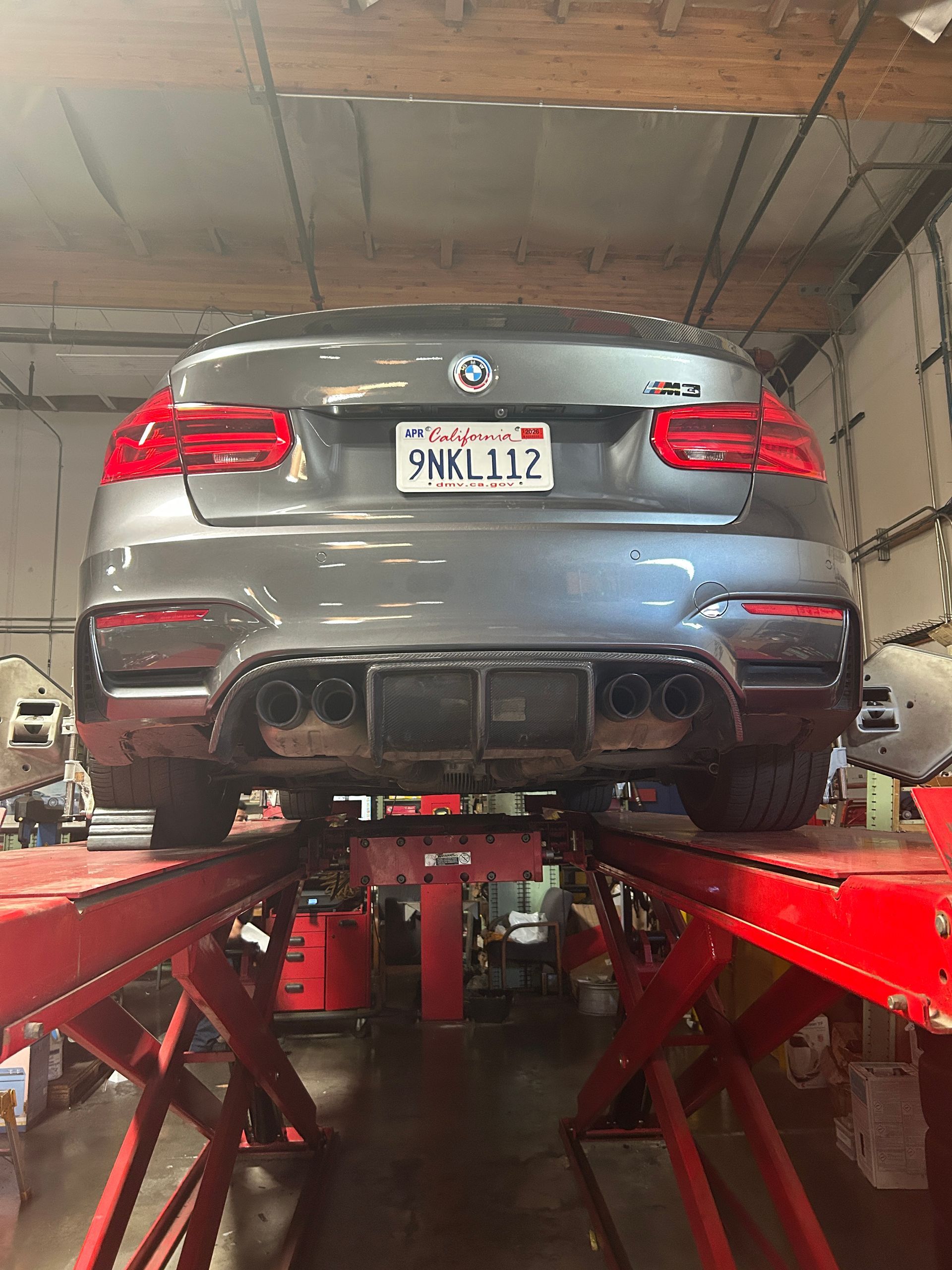 Silver BMW sedan on a red car lift in an auto repair shop, rear view with license plate visible