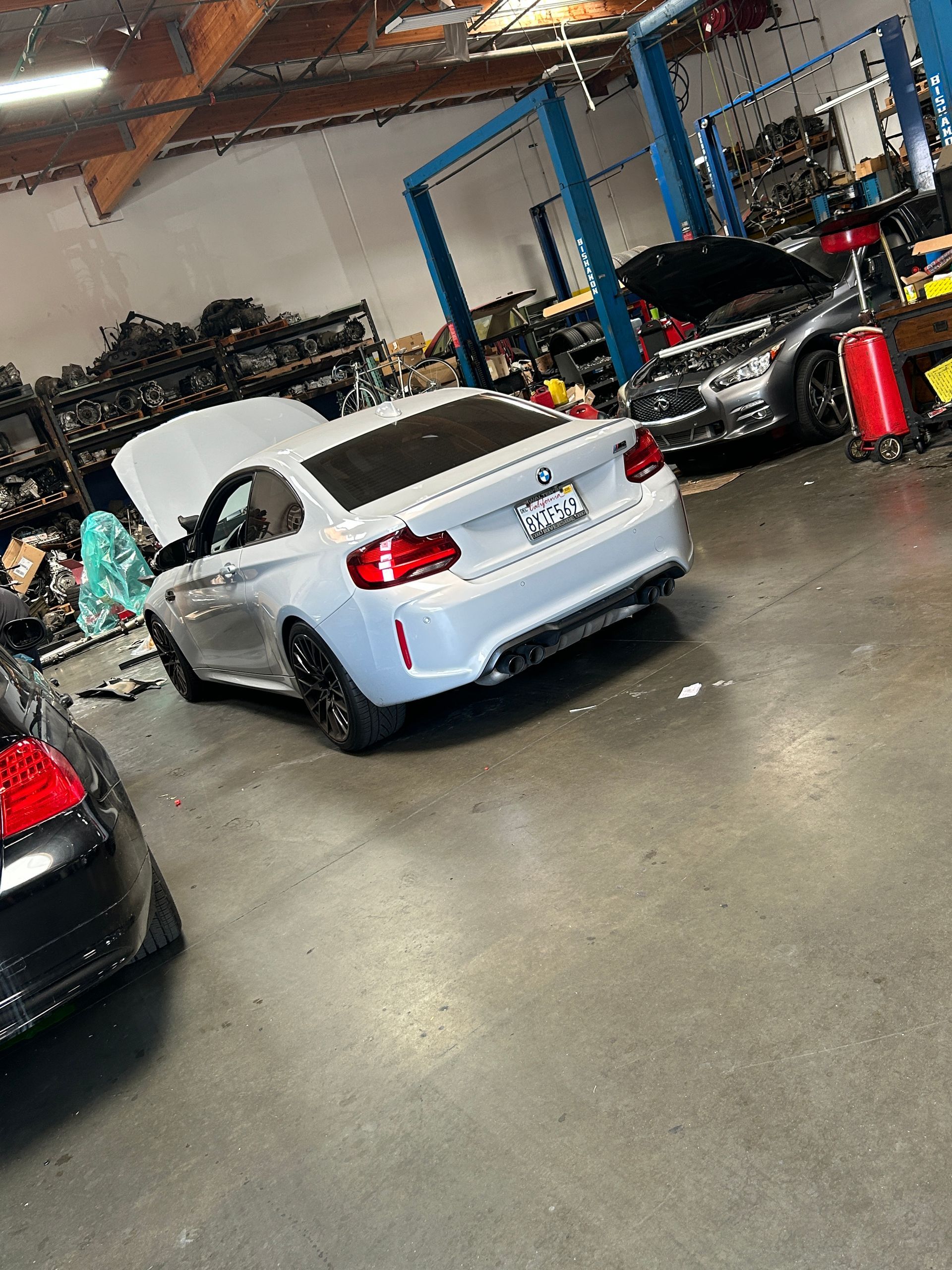 Silver BMW convertible in an auto shop garage, surrounded by other vehicles and tools.