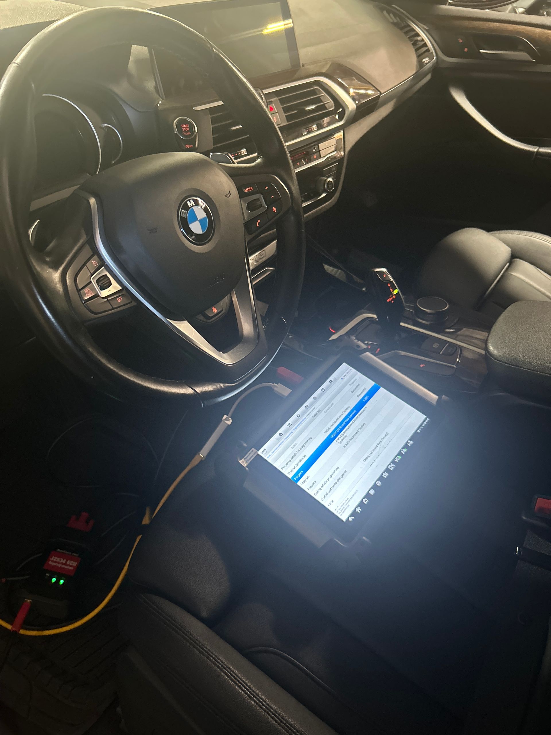 BMW car interior with a lit tablet on the seat and the dashboard visible at night