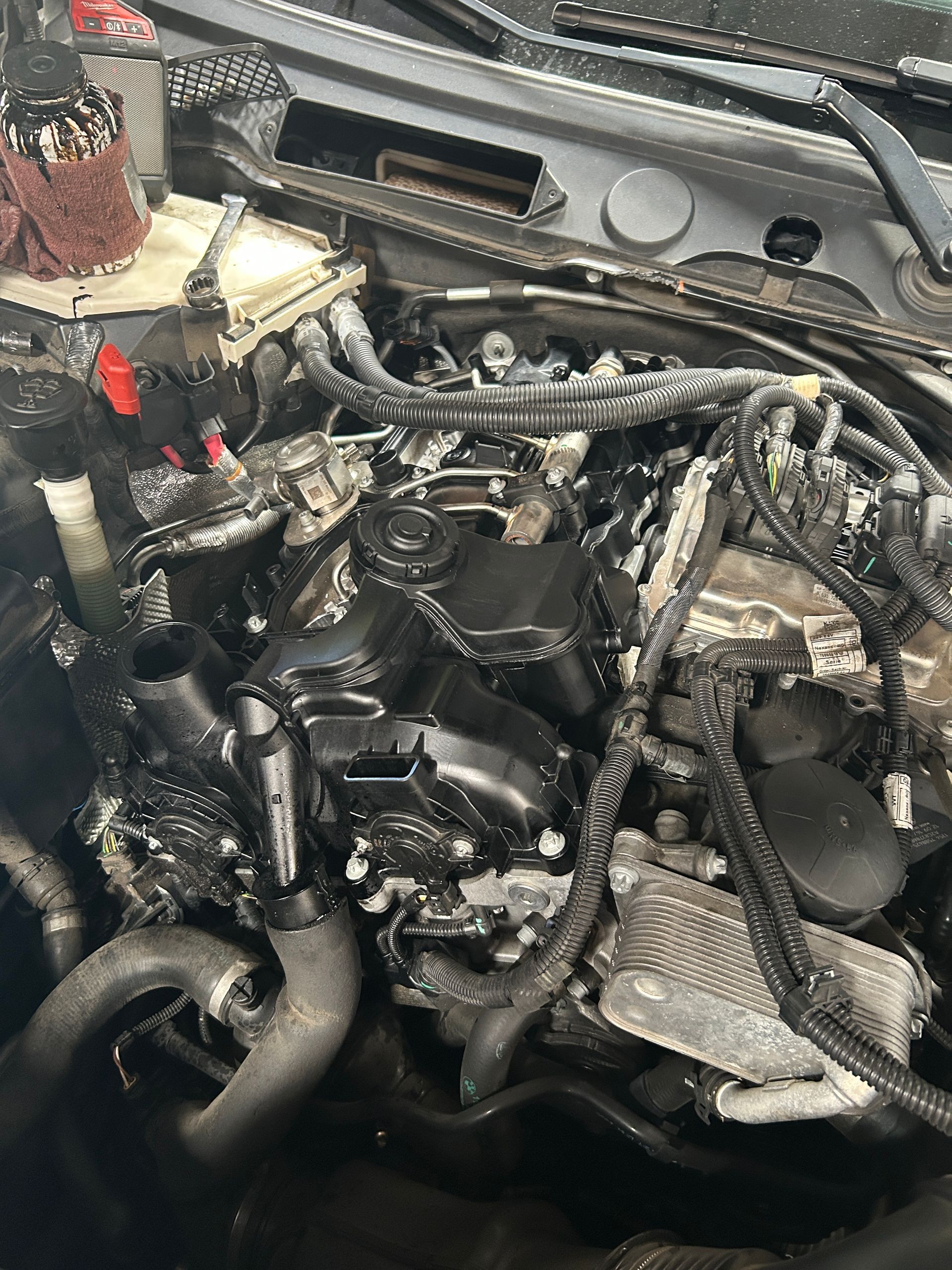 Open car engine bay with exposed wiring and hoses, showing heavy damage or disassembly.