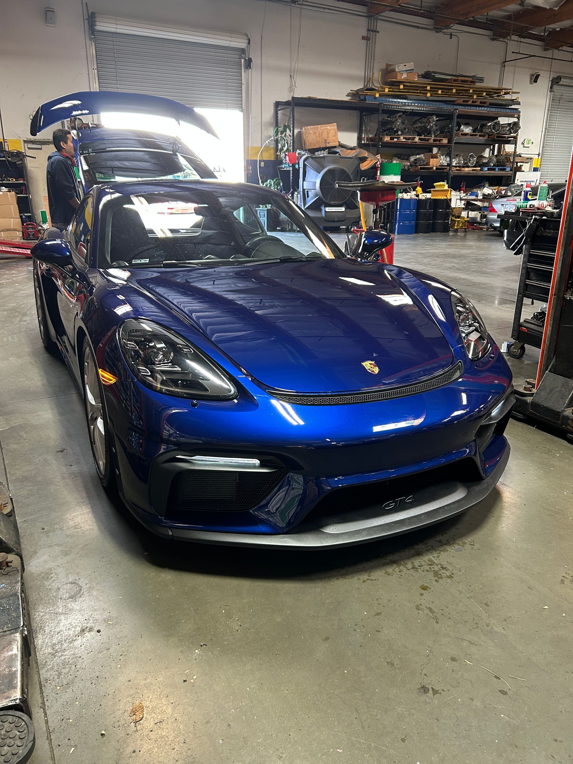 Blue sports car in an auto shop garage with mechanics and equipment in the background