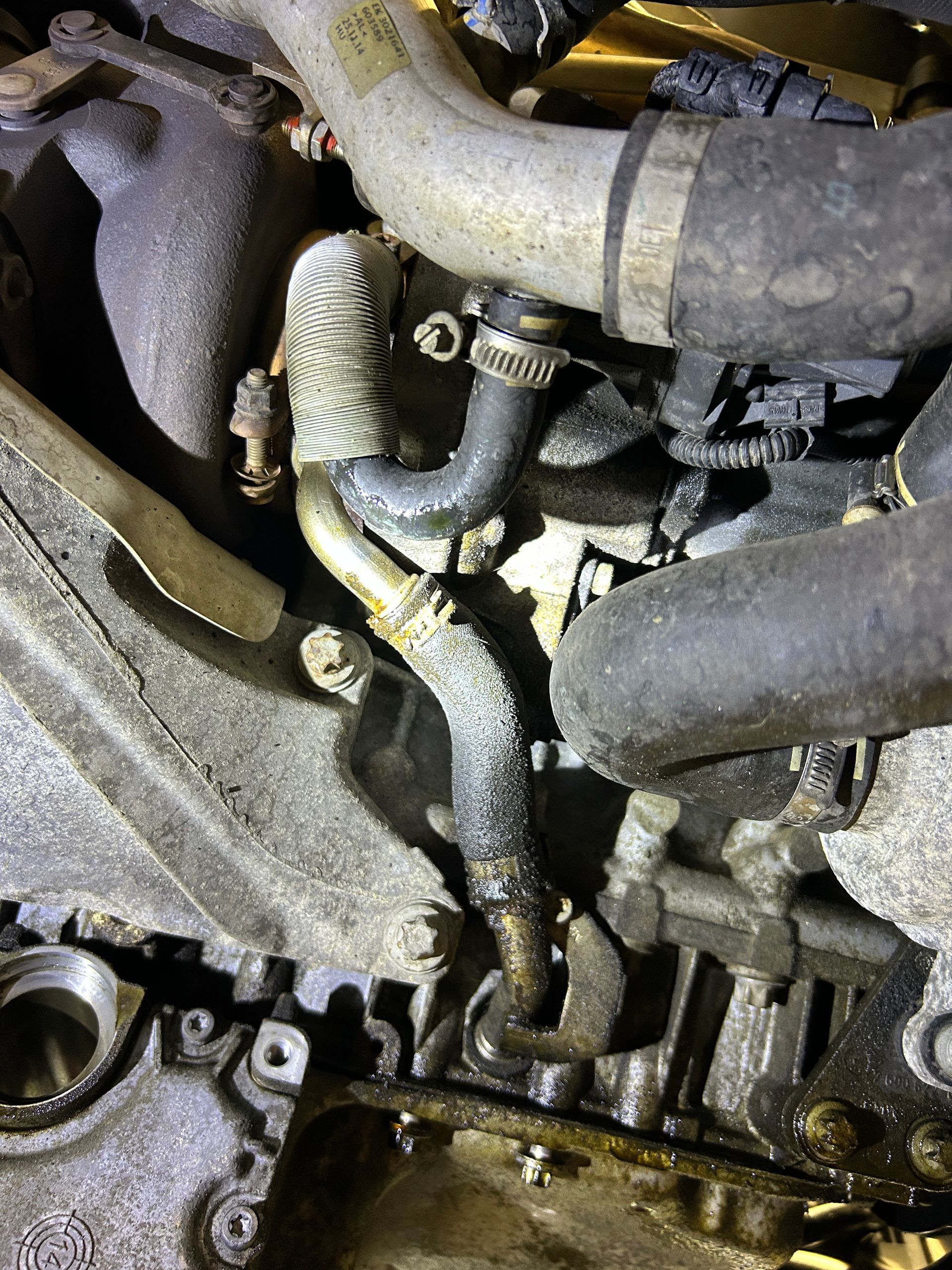 Close-up of tangled engine hoses and wiring, with a wrapped black line in a greasy car engine bay