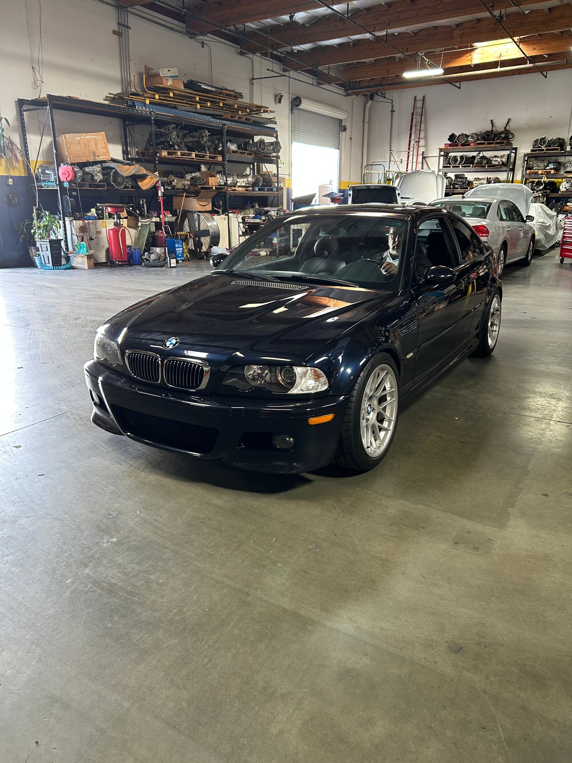 Black BMW sedan parked inside a garage with shelves and tools in the background