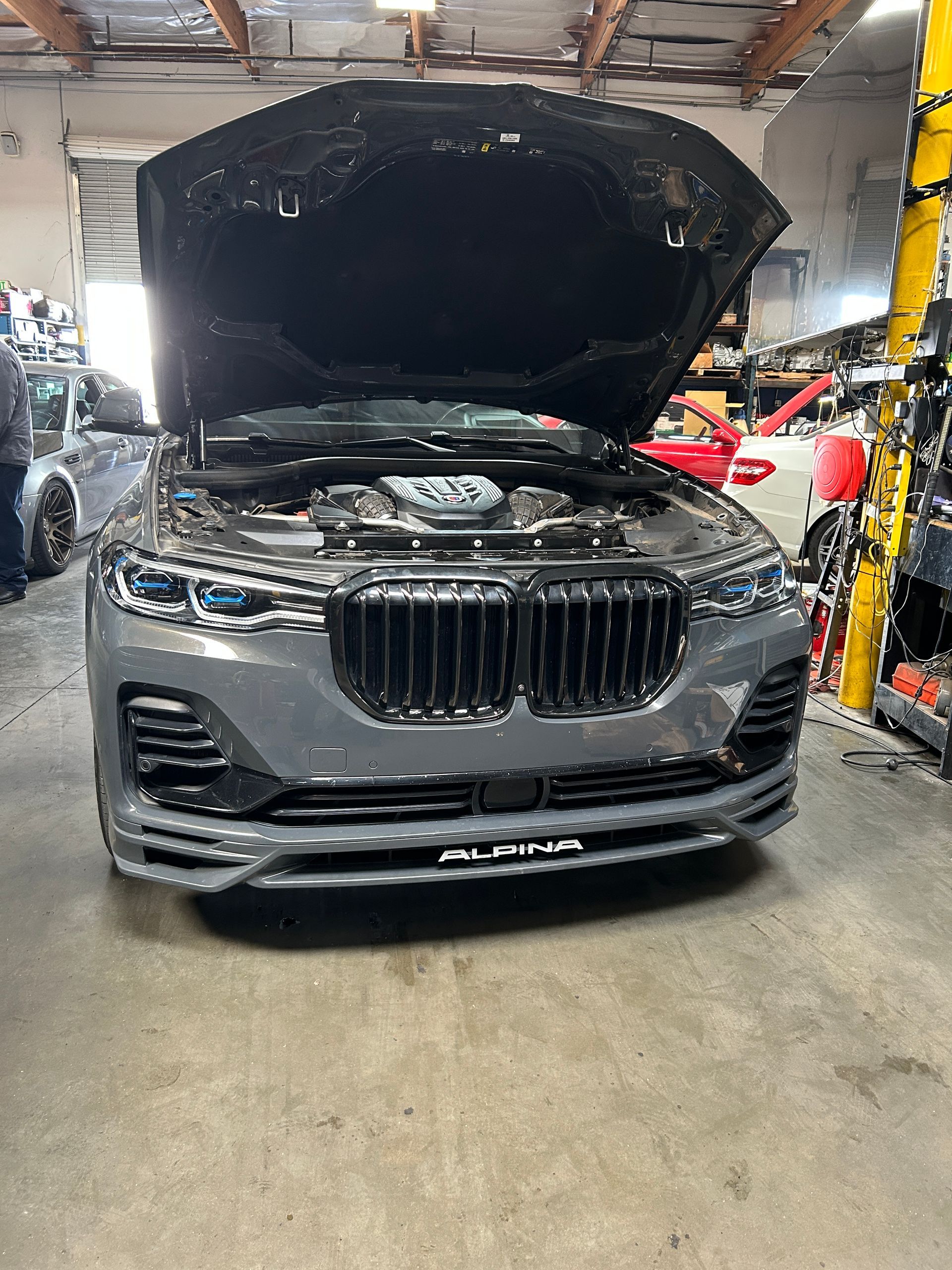 Gray BMW SUV with hood open in an auto repair shop, front view.