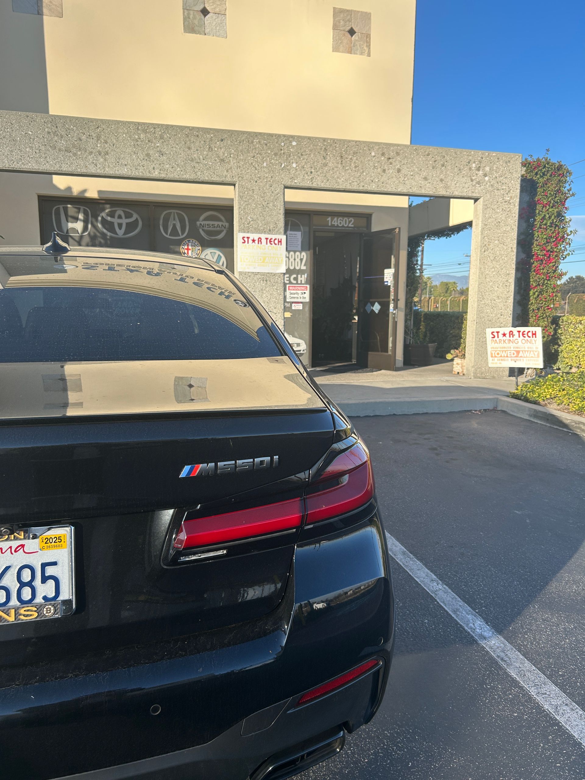 Black sedan parked outside a storefront with an open doorway and blue sky overhead