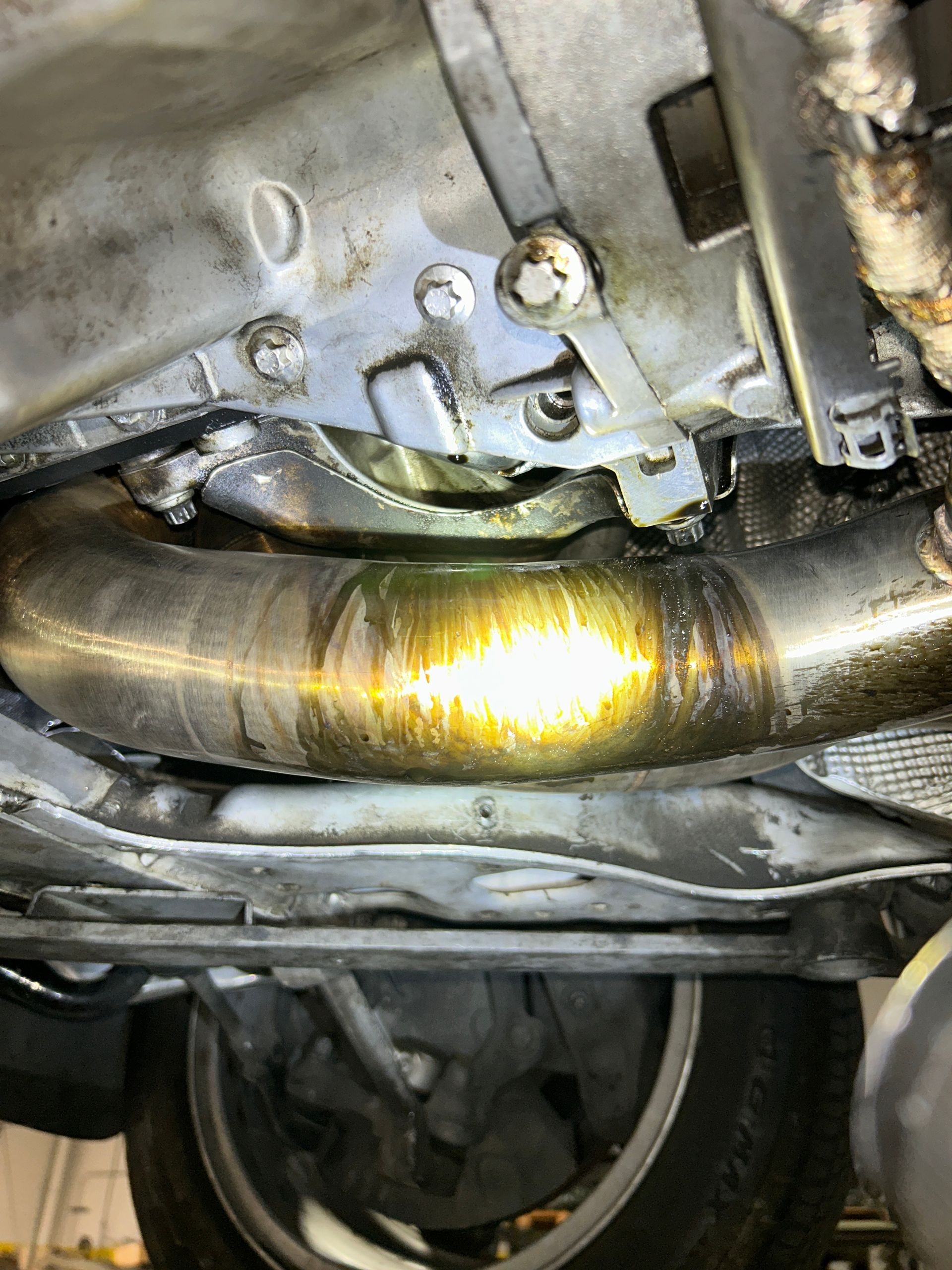 Close-up of a car’s undercarriage showing a shiny bent exhaust or pipe and nearby metal components
