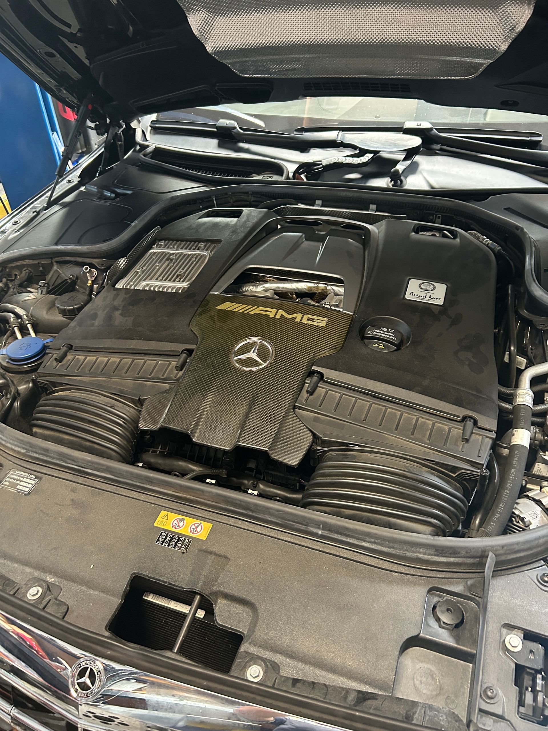 Mercedes-Benz engine bay with hood open, showing a black engine cover and gold detailing.