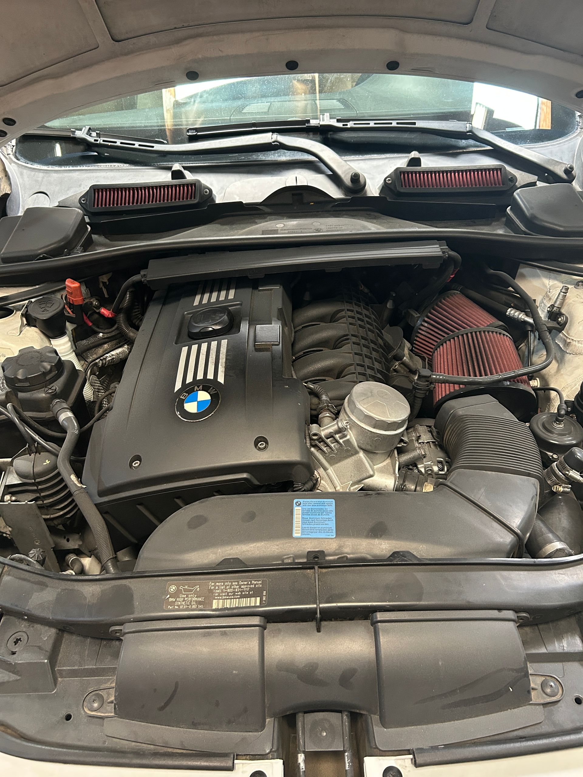 BMW engine bay with black engine cover, red intake filters, and hood open